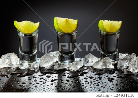 Tequila shots with lime slices on a wet black table. Tequila shots with lime slices on a wet black table. 124931110