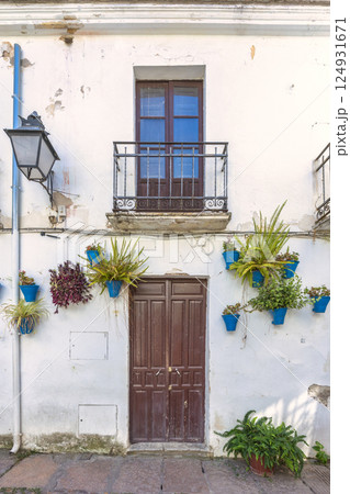 The Calleja de las Flores, popular tourist street of Cordoba city in Andalusia, Spain. Whitewashed building with brown door, balcony, and blue flower pots. A charming, rustic scene. The Calleja de las Flores, popular tourist street of Cordoba city in Andalusia, Spain. Whitewashed building with brown door, balcony, and blue flower pots. A charming, rustic scene. 124931671