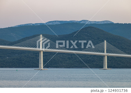 The Peljesac Bridge to Peljesac peninsula in Croatia, Europe. A long bridge stretches over calm water, connecting lush green hills under a tranquil sky. Landscape with modern architectural marvel. 124931736