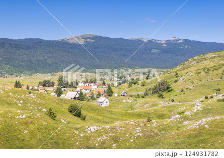 View of country in Bosnia and Herzegovina, Europe. Mountain village nestled in a green valley beneath a clear blue sky with distant hills and forests, showcasing a serene rural landscape. View of country in Bosnia and Herzegovina, Europe. Mountain village nestled in a green valley beneath a clear blue sky with distant hills and forests, showcasing a serene rural landscape. 124931782