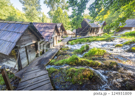 The Mlincici wooden watermills at Pliva river near Jajce town in Bosnia and Herzegovina, Europe. Rustic wooden huts line a flowing river connected by wooden walkways. The Mlincici wooden watermills at Pliva river near Jajce town in Bosnia and Herzegovina, Europe. Rustic wooden huts line a flowing river connected by wooden walkways. 124931809