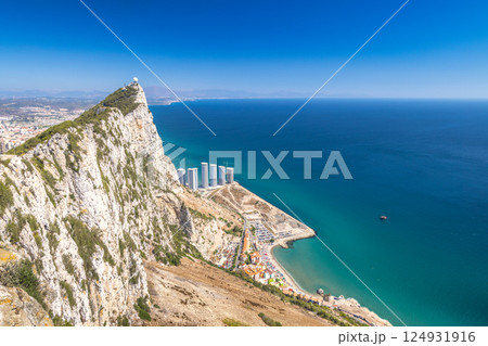 Gibraltar, British Overseas Territory and city on the Iberian Peninsula. Coastal cliffs and ocean view. Serene landscape with buildings and a clear blue sky. 124931916