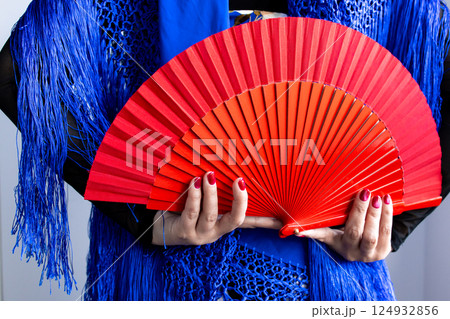 Female hands holding red fan with blue shawl in vibrant composition Female hands holding red fan with blue shawl in vibrant composition 124932856