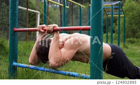 Young muscular athlete doing exercise on triceps at sport equipment outdoor. Male shirtless athlete working out at sport ground. Strong sporty man training at nature. Concept of healthy lifestyle 124932893