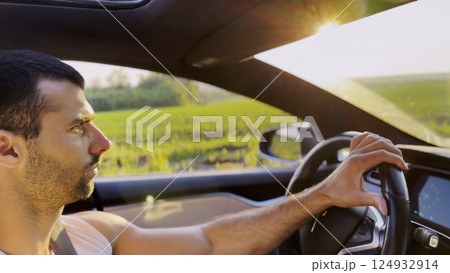 Profile of young handsome man driving a modern electric car with sunlight at background. Young male driver riding on electrical vehicle at countryside. Concept of journey and trip. Close up Profile of young handsome man driving a modern electric car with sunlight at background. Young male driver riding on electrical vehicle at countryside. Concept of journey and trip. Close up 124932914