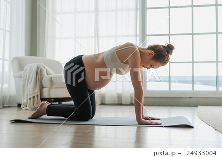 Pregnancy yoga fitness workout training. Pregnant woman practicing yoga at home. Pregnant girl doing sports exercise on yoga mat indoor. Woman with big belly have fitness training practicing asana 124933004