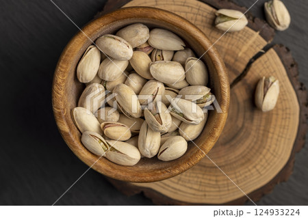pistachio in shells with added salt, unpeeled pistachio nuts in a wooden bowl with cracked shells pistachio in shells with added salt, unpeeled pistachio nuts in a wooden bowl with cracked shells 124933224