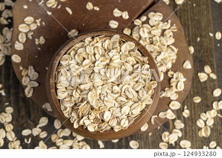 one bowl with oatmeal flakes for making porridge, scattered dry cereal flakes from oats flattened and steamed, top view one bowl with oatmeal flakes for making porridge, scattered dry cereal flakes from oats flattened and steamed, top view 124933280