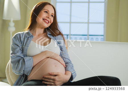 Pregnancy motherhood people expectation future. Pregnant woman touching big belly sitting on couch at home. Girl hugging her tummy enjoying pregnancy. Maternity tenderness parenthood new life concept 124933568