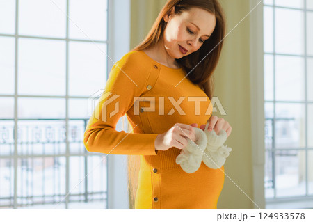 Pregnancy motherhood people expectation future. Pregnant woman with big belly holding newborn baby booties smiling at home. Young mom enjoying pregnancy. Maternity tenderness parenthood new life 124933578