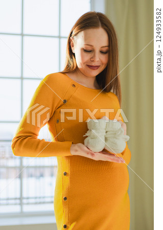Pregnancy motherhood people expectation future. Pregnant woman with big belly holding newborn baby booties smiling at home. Young mom enjoying pregnancy. Maternity tenderness parenthood new life Pregnancy motherhood people expectation future. Pregnant woman with big belly holding newborn baby booties smiling at home. Young mom enjoying pregnancy. Maternity tenderness parenthood new life 124933582