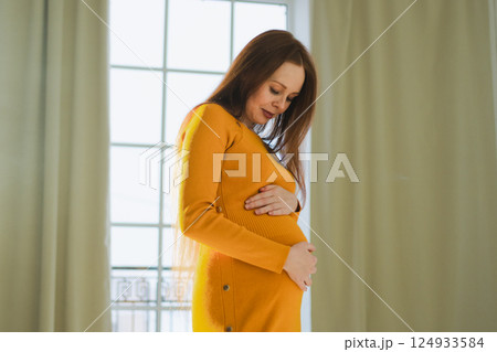 Pregnancy motherhood people expectation future. Pregnant woman with big belly standing near window at home. Girl hugging her tummy enjoying pregnancy. Maternity tenderness parenthood new life concept 124933584
