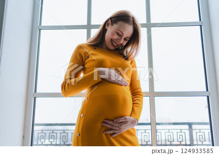 Pregnancy motherhood people expectation future. Pregnant woman with big belly standing near window at home. Girl hugging her tummy enjoying pregnancy. Maternity tenderness parenthood new life concept Pregnancy motherhood people expectation future. Pregnant woman with big belly standing near window at home. Girl hugging her tummy enjoying pregnancy. Maternity tenderness parenthood new life concept 124933585