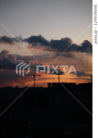 Construction cranes silhouetted against a colorful sunset in the city 124934098
