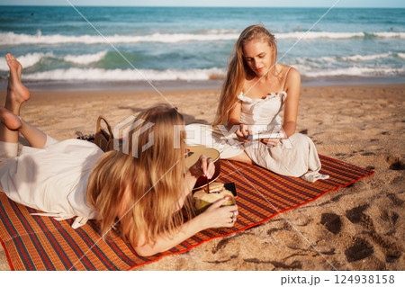 Two Women Sipping Coconut and Enjoying a Book on the Beach 124938158