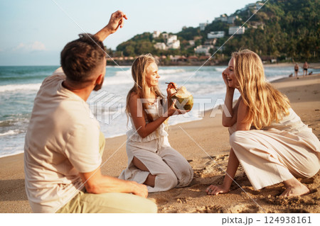 Friends Unwinding on the Beach with Refreshing Coconut Friends Unwinding on the Beach with Refreshing Coconut 124938161