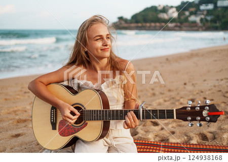 Woman Playing Guitar and Relaxing on the Beach at Sunset Woman Playing Guitar and Relaxing on the Beach at Sunset 124938168