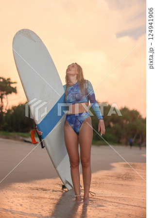 A woman wearing a bikini is standing on the beach while holding a surfboard A woman wearing a bikini is standing on the beach while holding a surfboard 124941906