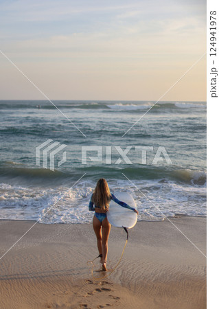 A woman is leisurely walking along the beach while holding a surfboard A woman is leisurely walking along the beach while holding a surfboard 124941978