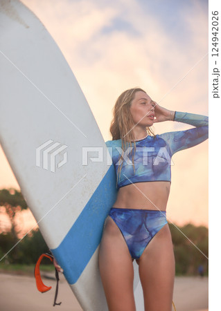 A woman wearing a bikini is standing on the beach while holding a surfboard 124942026
