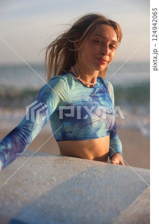 A Surfer Girl Happily Enjoying the Beautiful Sunset on the Beach by the Gentle Ocean Waves 124942065