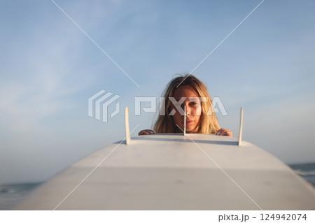 A woman is joyfully surfing at sunset with her surfboard against a clear blue sky 124942074