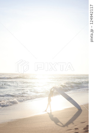 A person is standing on a sandy beach while holding a surfboard 124942117