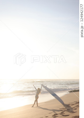 A person is standing on a sandy beach while holding a surfboard 124942177