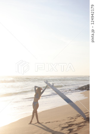 A person is standing on a sandy beach while holding a surfboard 124942179