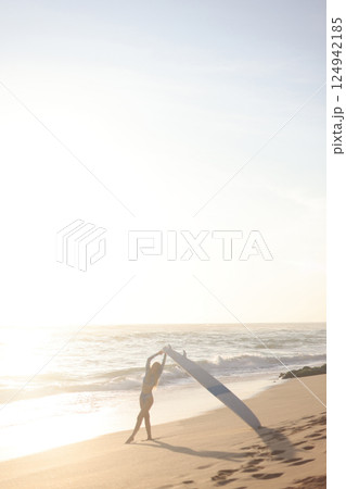 A person is standing on a sandy beach while holding a surfboard 124942185