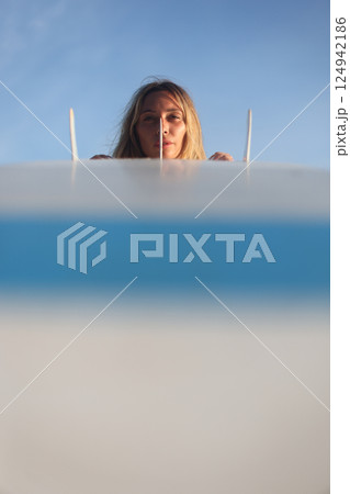 A woman is joyfully surfing at sunset with her surfboard against a clear blue sky 124942186