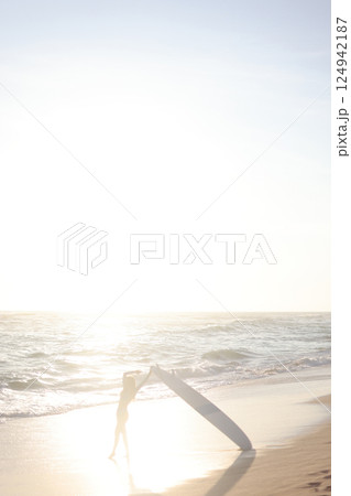 A person is standing on a sandy beach while holding a surfboard 124942187