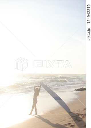 A person is standing on a sandy beach while holding a surfboard 124942210