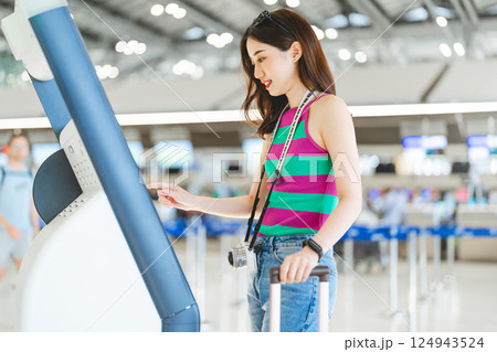 Woman passenger with travel luggage Using self service check in KIOSK at airport terminal 124943524