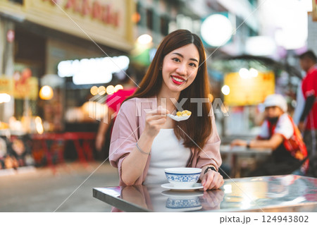Young adult asian woman eating chinese dessert menu sitting at street food table travel china town Young adult asian woman eating chinese dessert menu sitting at street food table travel china town 124943802