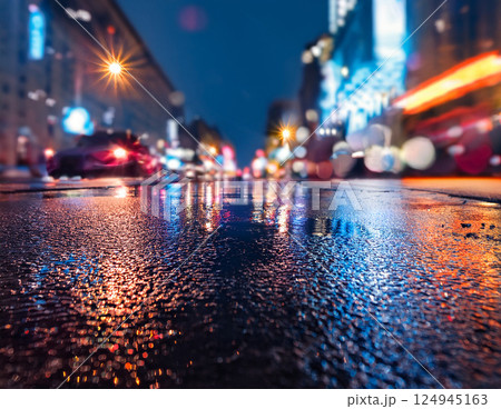雨の夜の都市、ネオンが反射する濡れた舗道のクローズアップ 124945163