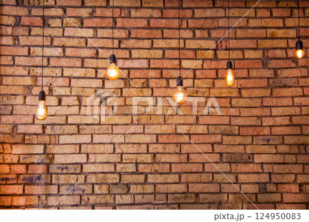 Old electric incandescent lamps with tungsten filament. Against the backdrop of a brick wall. Texture of old stone background. 124950083