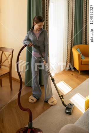 Woman vacuuming living room carpet while wearing cozy slippers in modern apartment during daylight 124952327