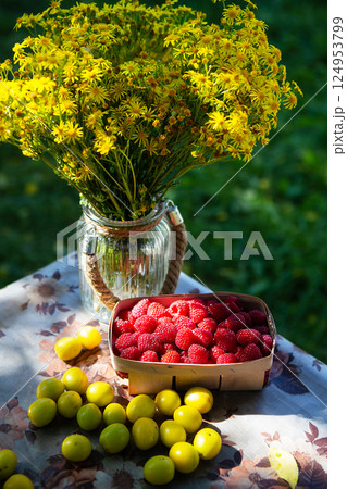 Fresh sweet juicy raspberries in a wooden basket on a wooden table lie along with yellow cherry plum. Beautiful sunset light. 124953799