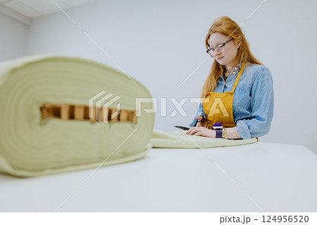 female seamstress cuts product from a roll of fabric in sewing workshop. fashion industry. female seamstress cuts product from a roll of fabric in sewing workshop. fashion industry. 124956520