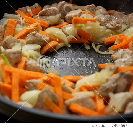 Steam rises above the frying pan from the frying meat with chopped onions and carrots 124956675