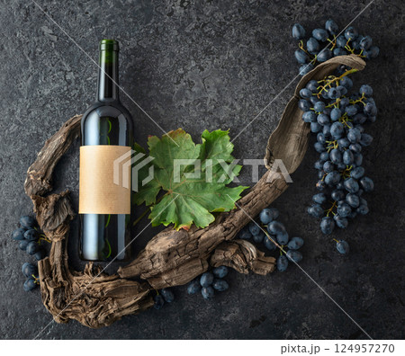 Bottle of red wine, blue grapes, and old vine snags on a black stone background. 124957270