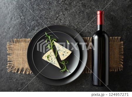 Bottle of red wine and blue cheese on a black plate. 124957271