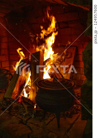 Open fire in the fireplace. A stove in which food is cooked. Cast-iron cauldrons for cooking at the stake. Firewood in the fireplace. Cozy home atmosphere. Night. Open fire in the fireplace. A stove in which food is cooked. Cast-iron cauldrons for cooking at the stake. Firewood in the fireplace. Cozy home atmosphere. Night. 124957600
