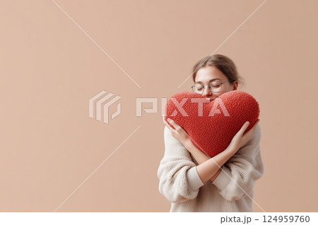 A young woman embraces a large heart-shaped pillow, radiating warmth and affection. A young woman embraces a large heart-shaped pillow, radiating warmth and affection. 124959760
