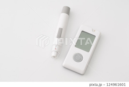 Blood glucose meter and lancet pen on white background, used for diabetes monitoring and blood sugar level testing. 124961601