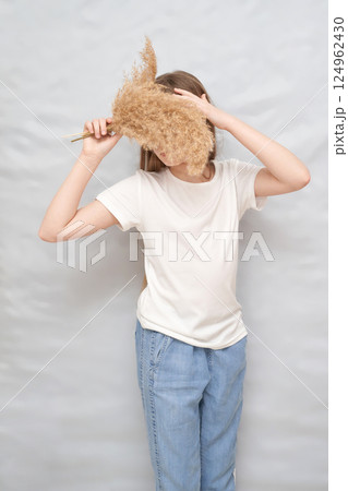 Young caucasian female hiding face with dried wheat stalks in casual attire Young caucasian female hiding face with dried wheat stalks in casual attire 124962430