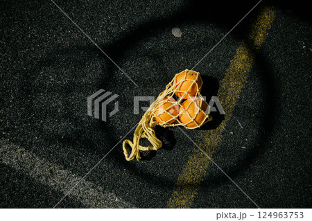 A bag filled with fresh oranges is laying on the ground in a circle 124963753