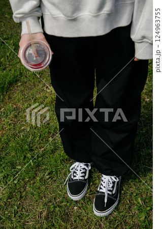 A person stands on green grass, holding a cup of soda 124963755
