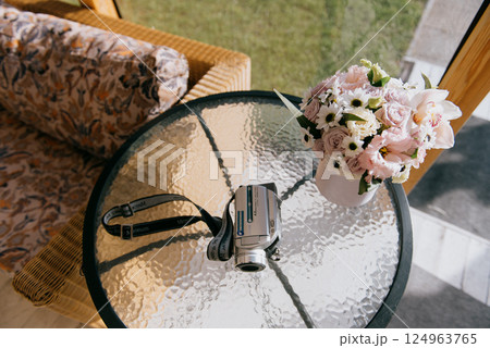 A camera is on a glass table next to a vase of fresh flowers 124963765